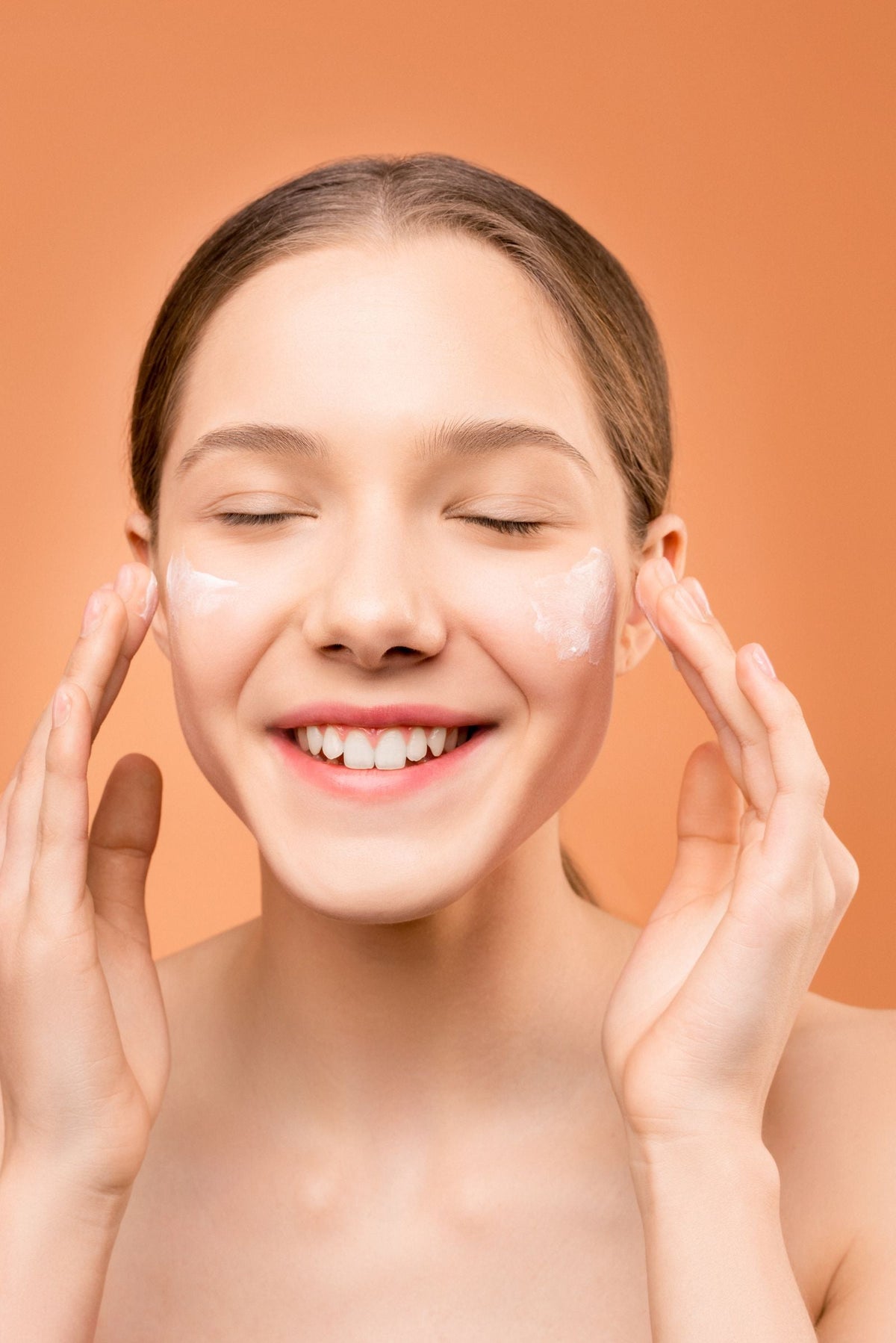 Woman smiling while applying moisturiser to her face