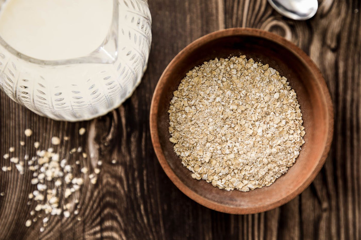 A wooden bowl of oats with a jug of milk