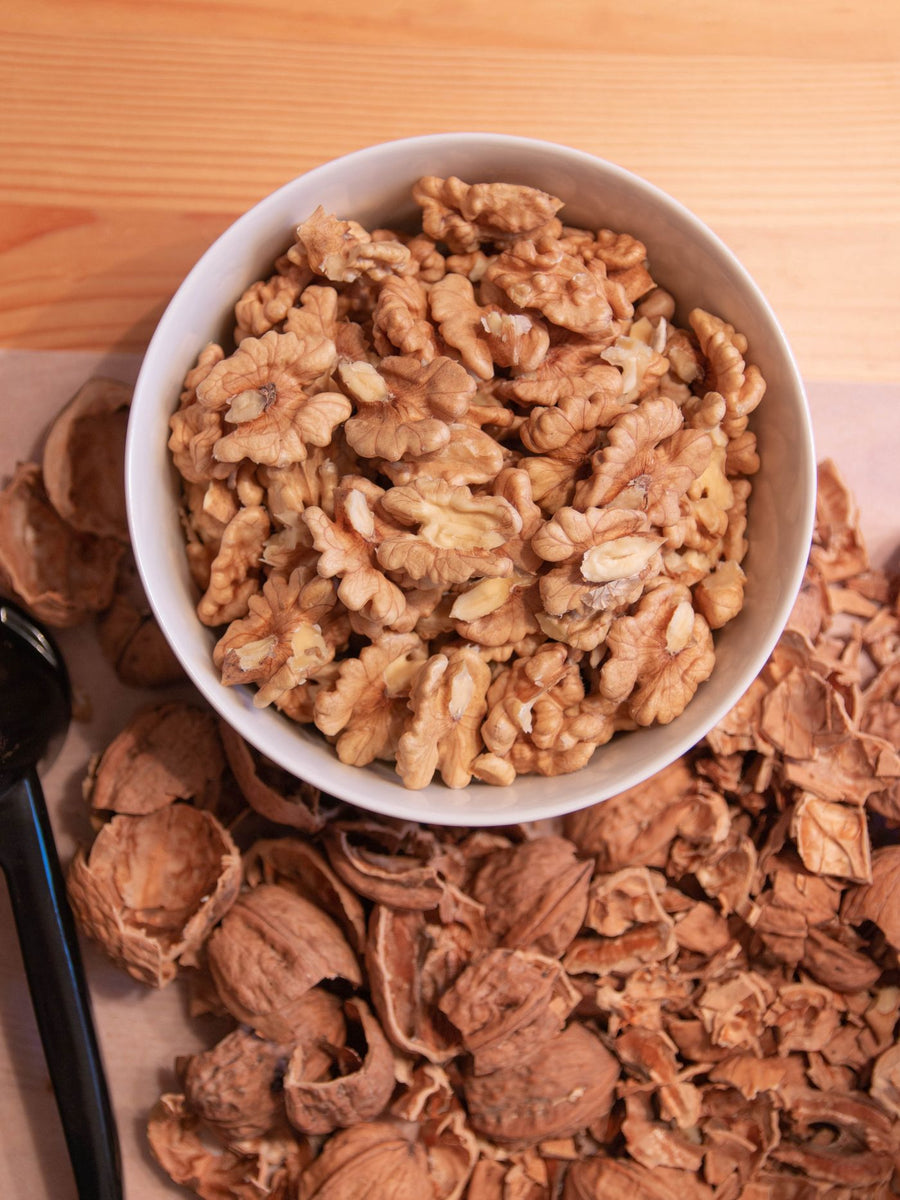 A bowl of shelled walnuts surrounded by walnut shells